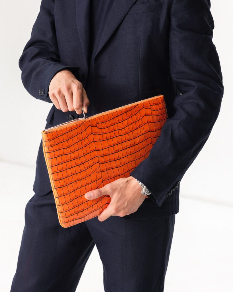 Man holding an orange crocodile-embossed Etier leather pouch, showcasing premium craftsmanship and luxury design.
