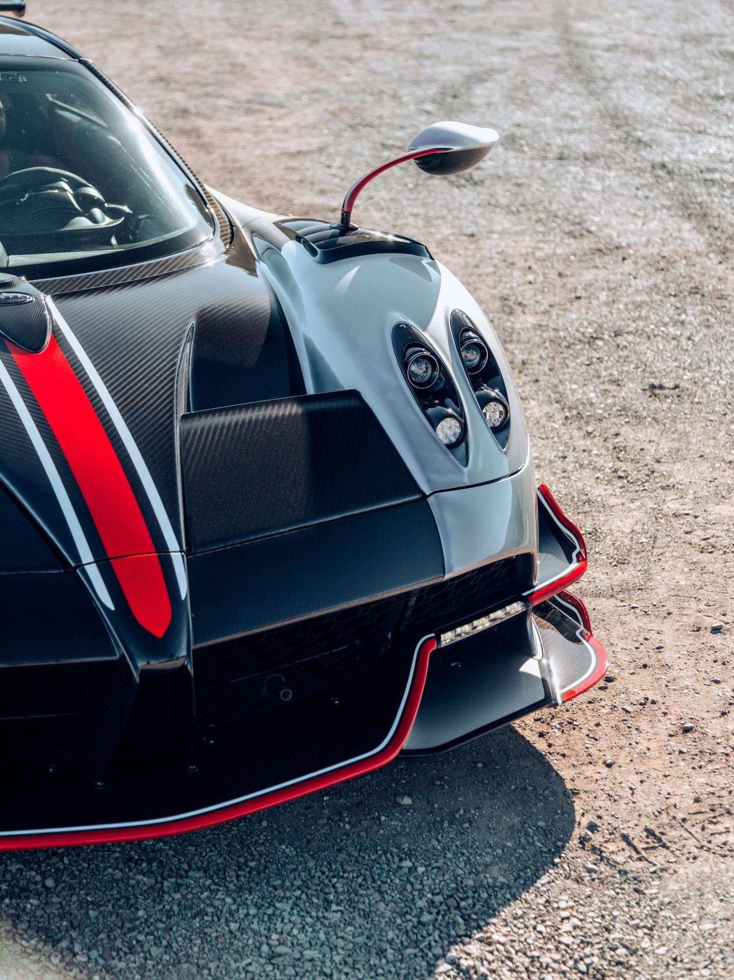 Pagani hypercar front detail showcasing carbon fibre bodywork, red accent stripe and quad headlight design