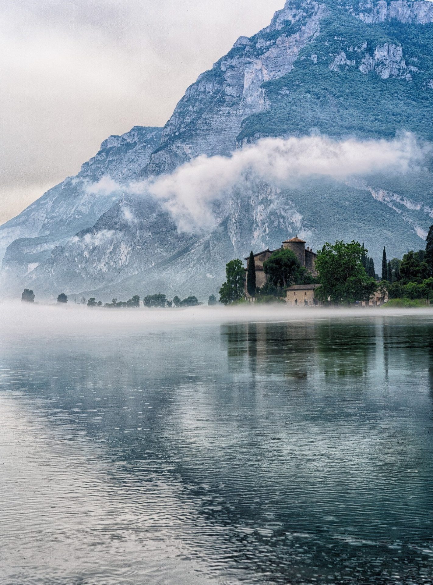 Misty morning over Lake Garda with mountains reflected in still water