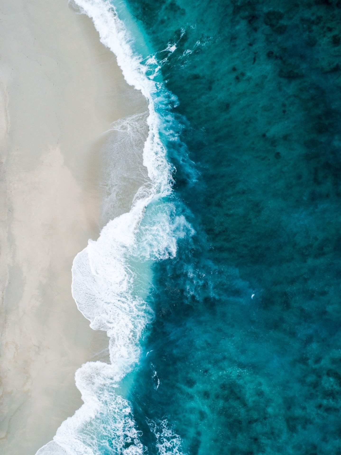 Aerial view of turquoise waves meeting pristine sandy beach on Necker Island