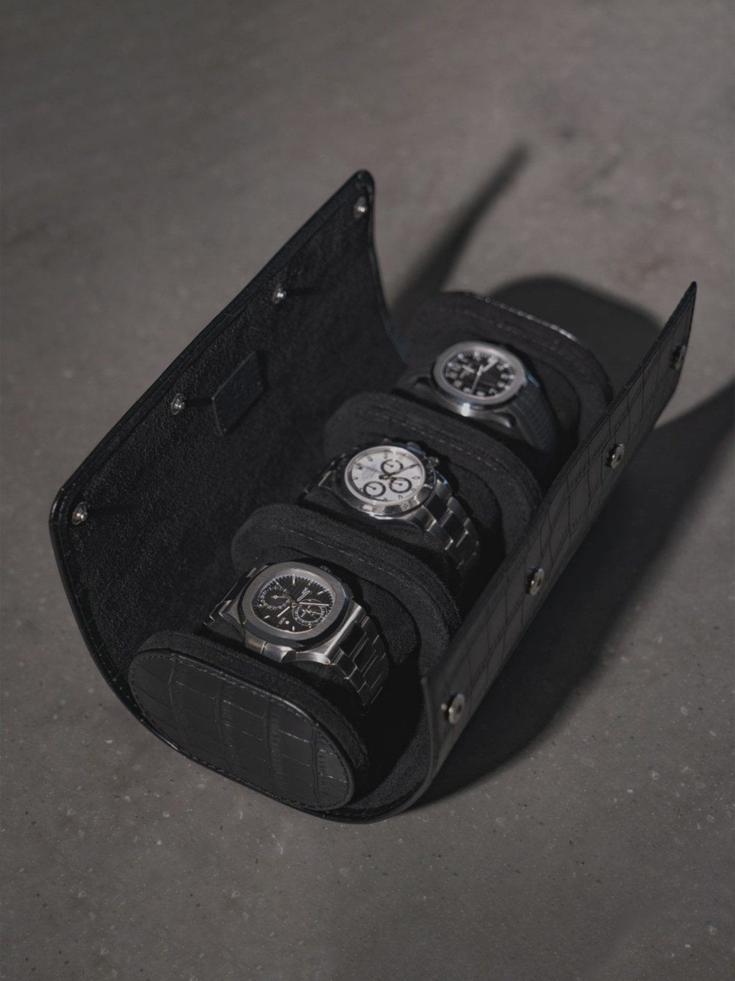 Black crocodile-embossed leather watch roll holding three luxury watches